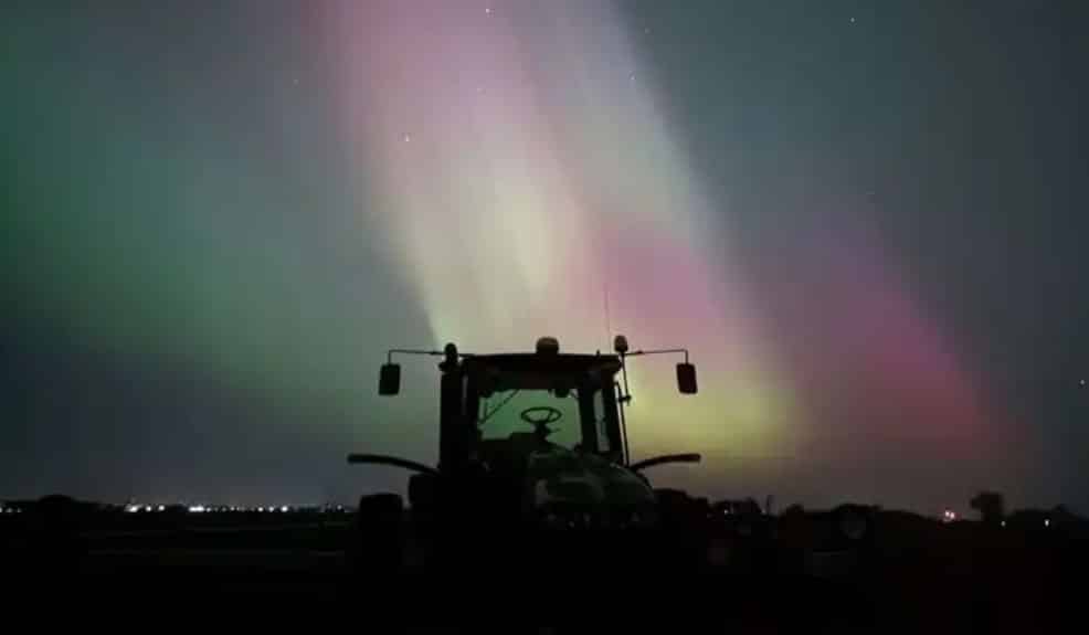 Northern lights over a tractor in a farm field