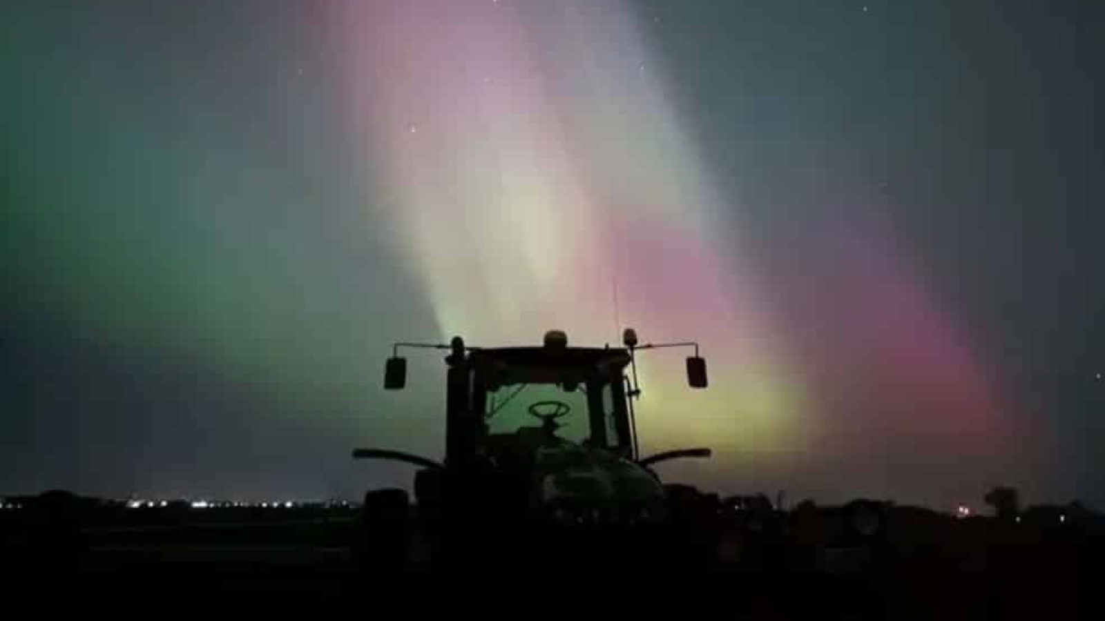 Northern lights over a tractor in a farm field